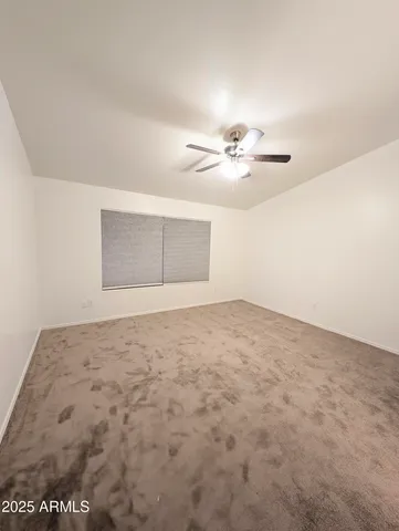 an empty room with a chandelier fan and windows