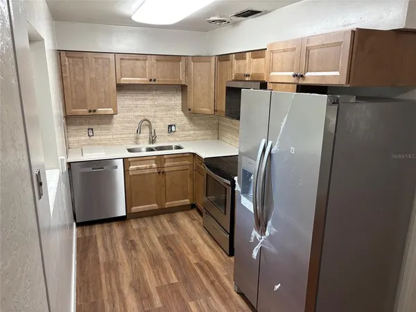 a kitchen with stainless steel appliances granite countertop a refrigerator a sink dishwasher a stove and white countertops with wooden floor