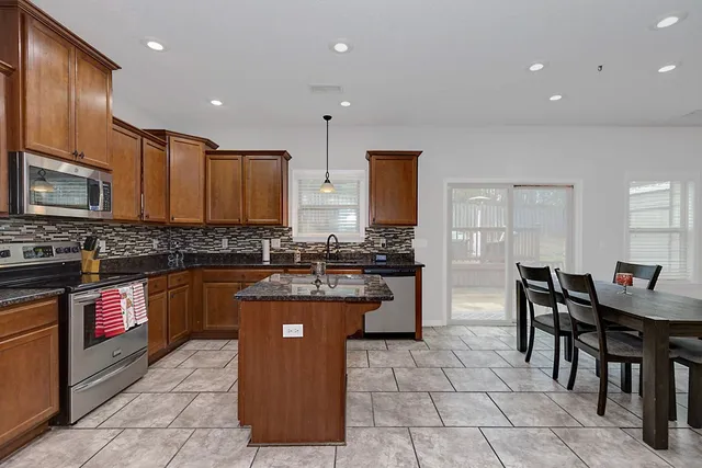 a kitchen with stainless steel appliances granite countertop a stove top oven a sink a dining table and chairs