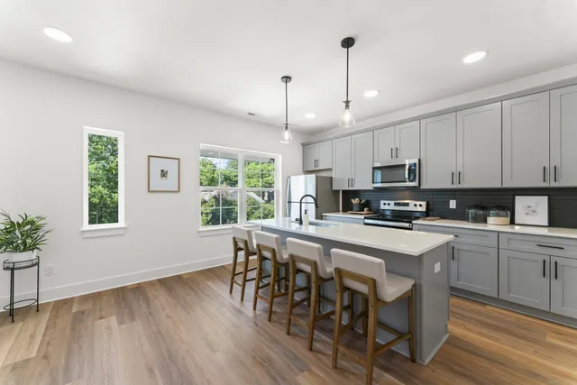 a kitchen with stainless steel appliances granite countertop a stove a refrigerator a sink dishwasher a dining table and chairs with wooden floor