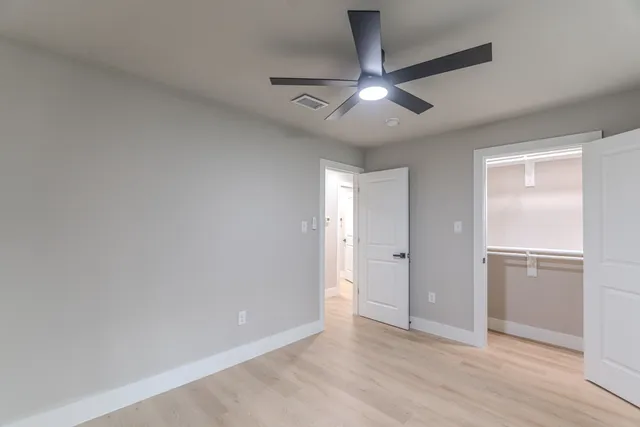 an empty room with wooden floor ceiling fan and windows