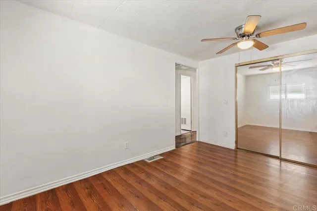 an empty room with wooden floor fan and windows