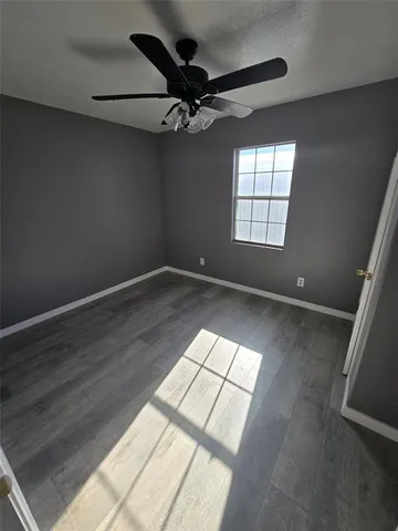 an empty room with wooden floor fan and windows