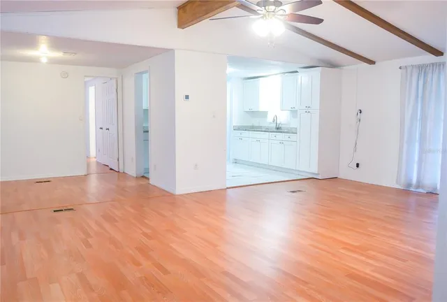 a view of an empty room with wooden floor and a ceiling fan