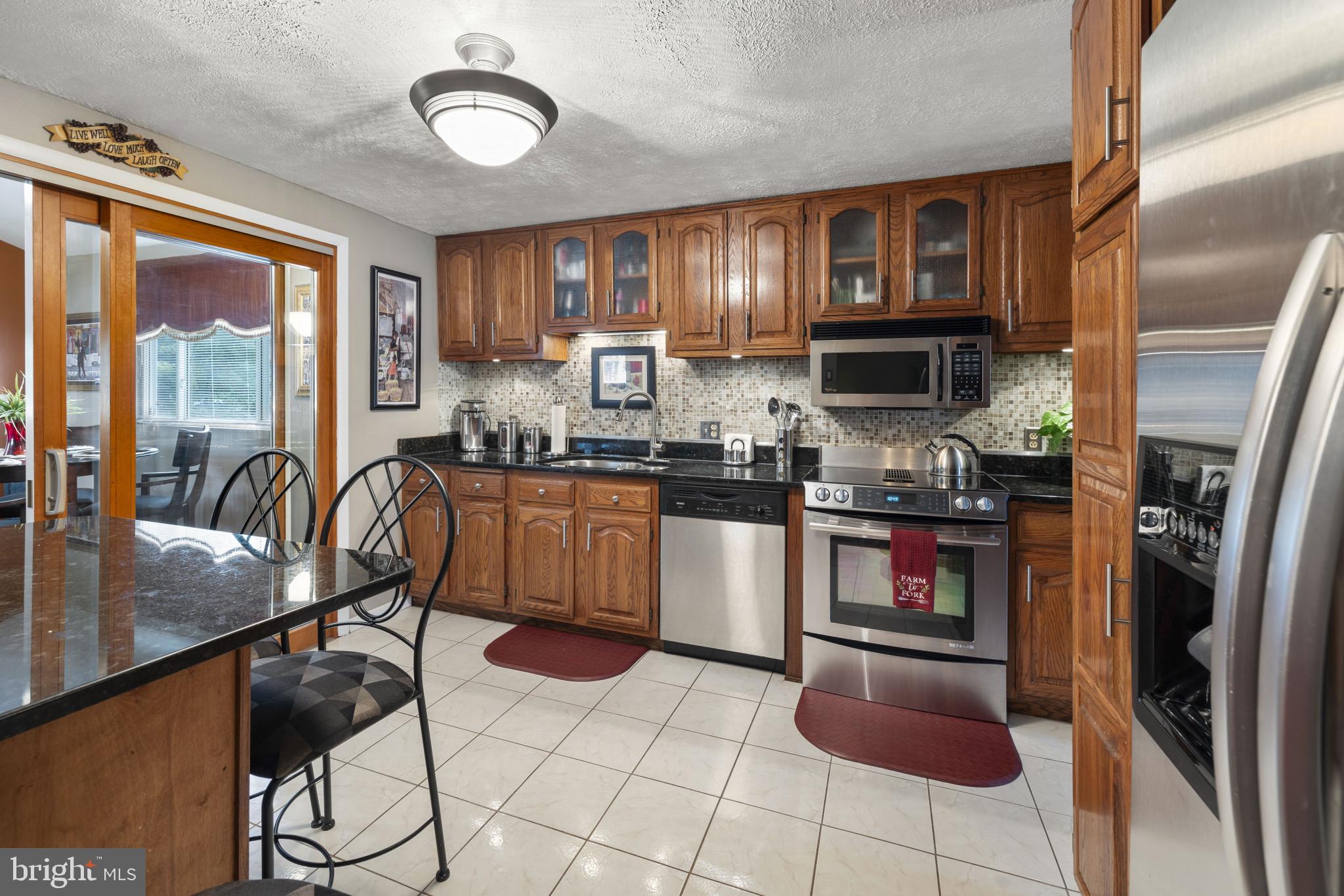 4105 Hanwell Road Randallstown, MD 21133 - Photo 16 of 37 a kitchen with stainless steel appliances granite countertop a stove top oven a sink a dining table and chairs with wooden floor