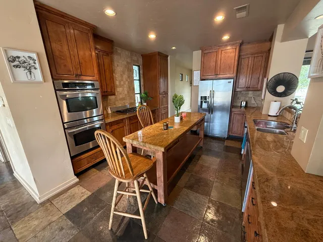 a kitchen with stainless steel appliances kitchen island granite countertop a table chairs and a refrigerator