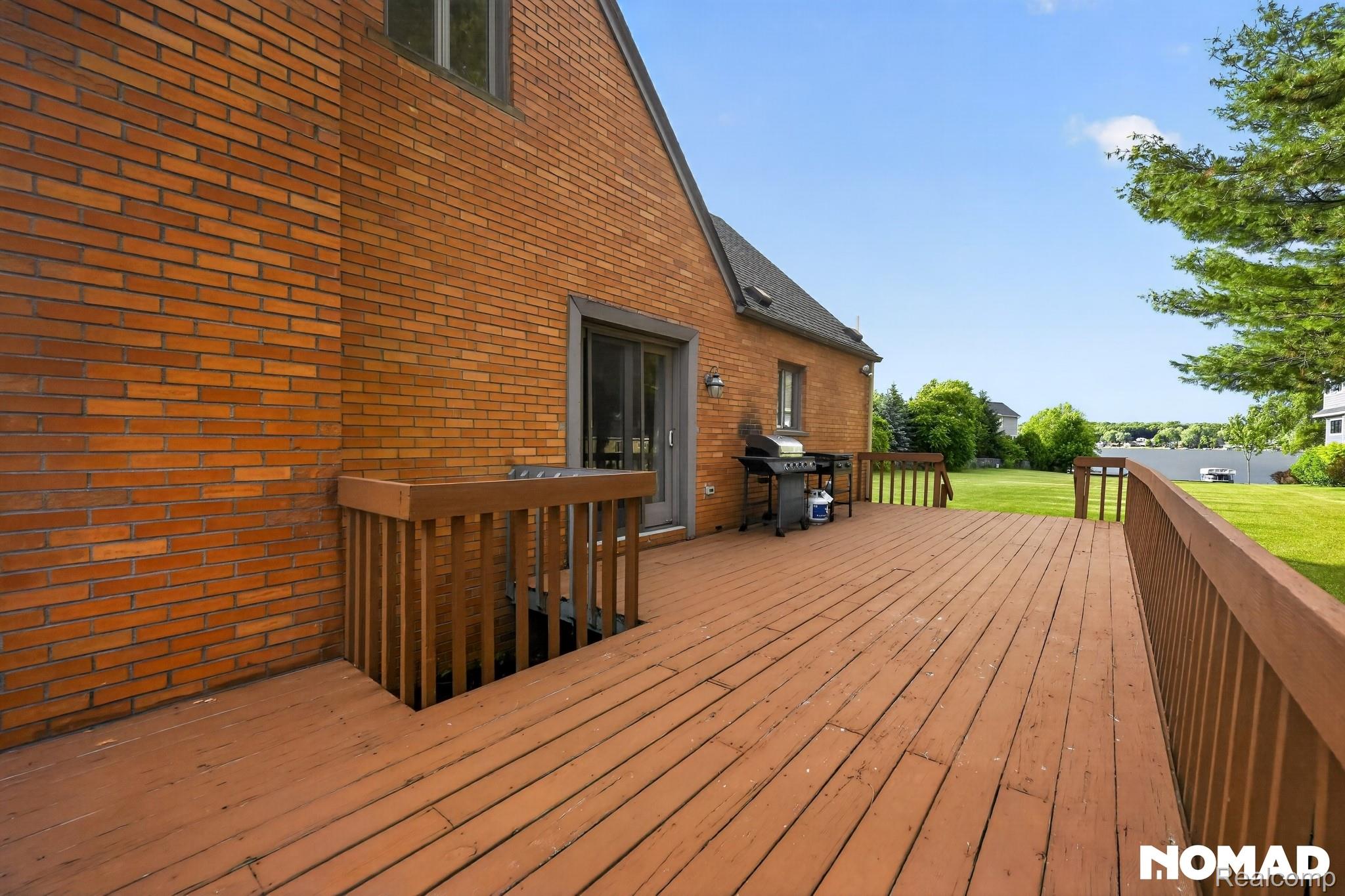 8315 Hilton Road Brighton, MI 48114 - Photo 4 of 26 Spacious wooden deck with a built-in railing, featuring a sliding glass door entry to the brick-sided residence and overlooking a large grassy yard