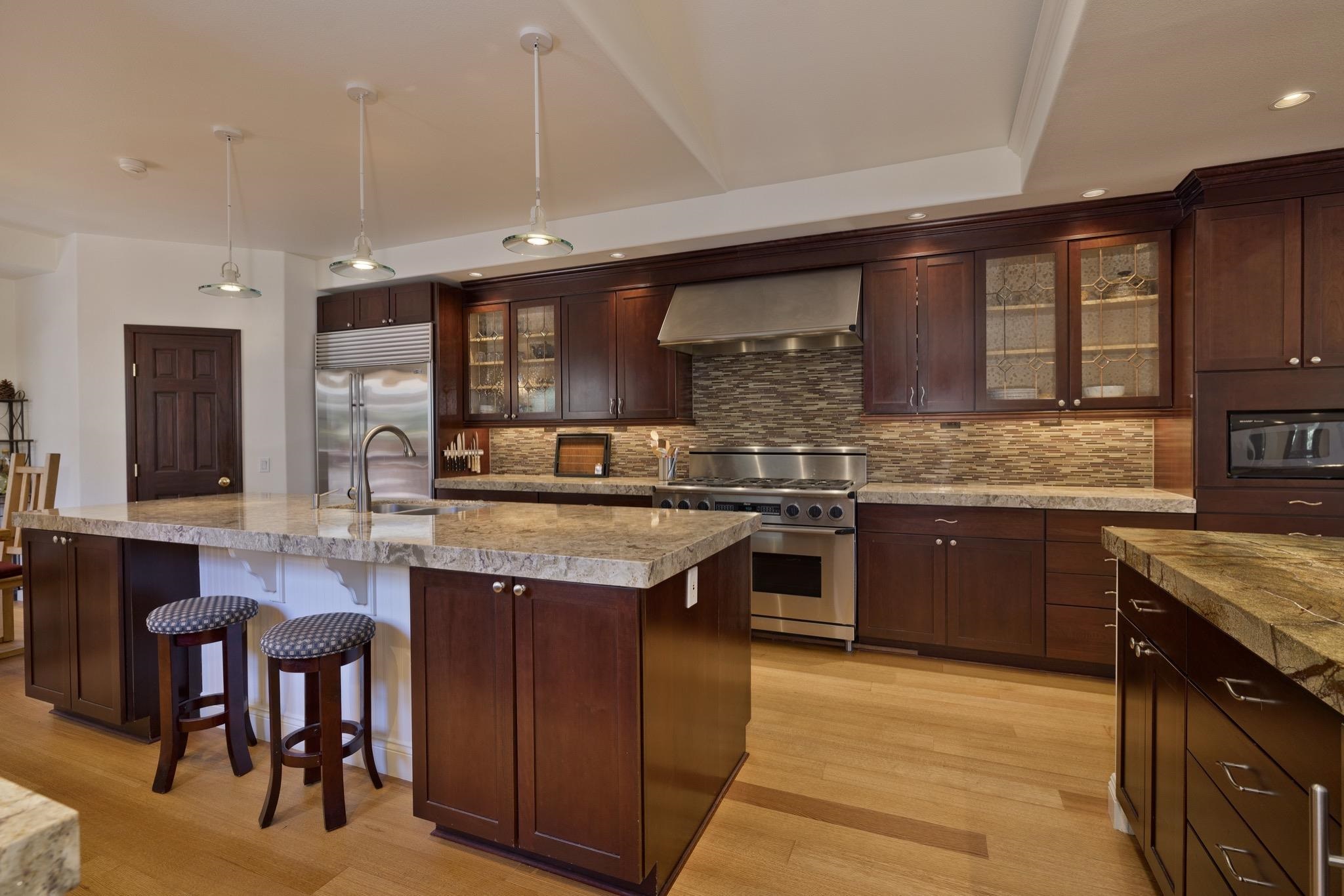378 Ridge Way Mammoth Lakes, CA 93546 - Photo 9 of 43 Gourmet kitchen featuring a large island with seating, stainless steel appliances, dark wood cabinetry, a tiled backsplash, and light wood-finish flooring