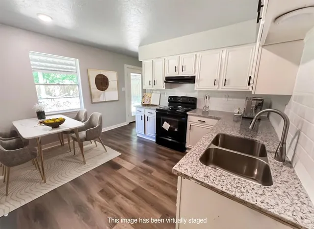 a kitchen with stainless steel appliances kitchen island granite countertop a sink a stove top oven a dining table and chairs with wooden floor