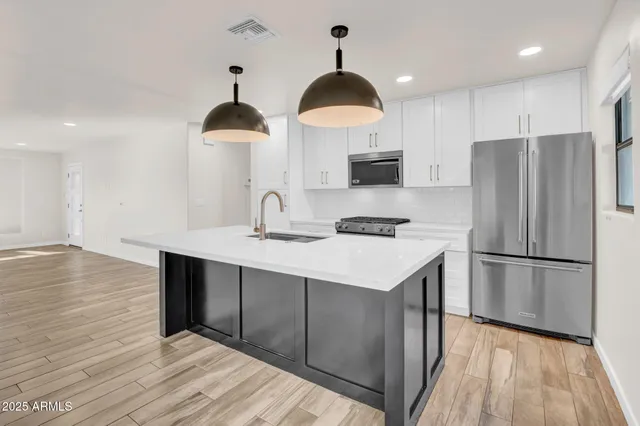 a kitchen with stainless steel appliances a stove a refrigerator a sink wooden floor and cabinets