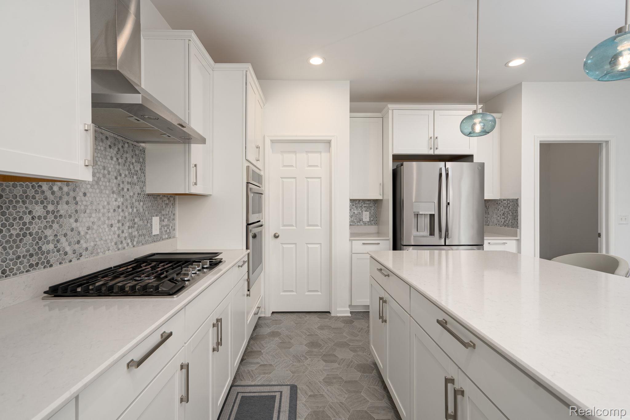 48904 Carnegie Way Macomb, MI 48042 - Photo 11 of 34 Kitchen featuring white shaker cabinetry, stainless steel appliances, a gas range with a matching vent hood, an extended kitchen island with a light-colored countertop, and a mosaic tile backsplash