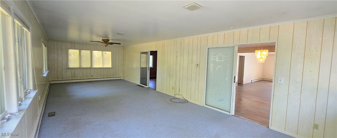 2707 Merriweather Road Sandusky, OH 44870 - Photo 17 of 28 Spare room featuring ceiling fan with notable chandelier, a wealth of natural light, wooden walls, and a baseboard radiator