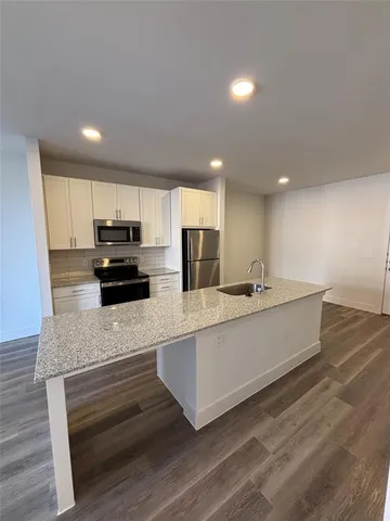 a large white kitchen with kitchen island a sink dishwasher a refrigerator and a stove with wooden floor