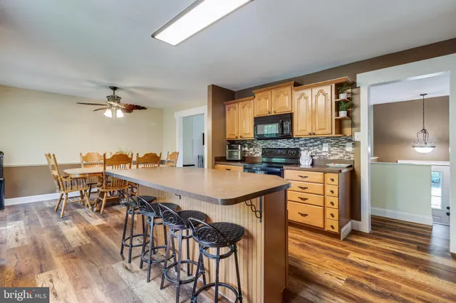 a open kitchen with stainless steel appliances granite countertop a stove top oven a refrigerator a dining table and chairs with wooden floor