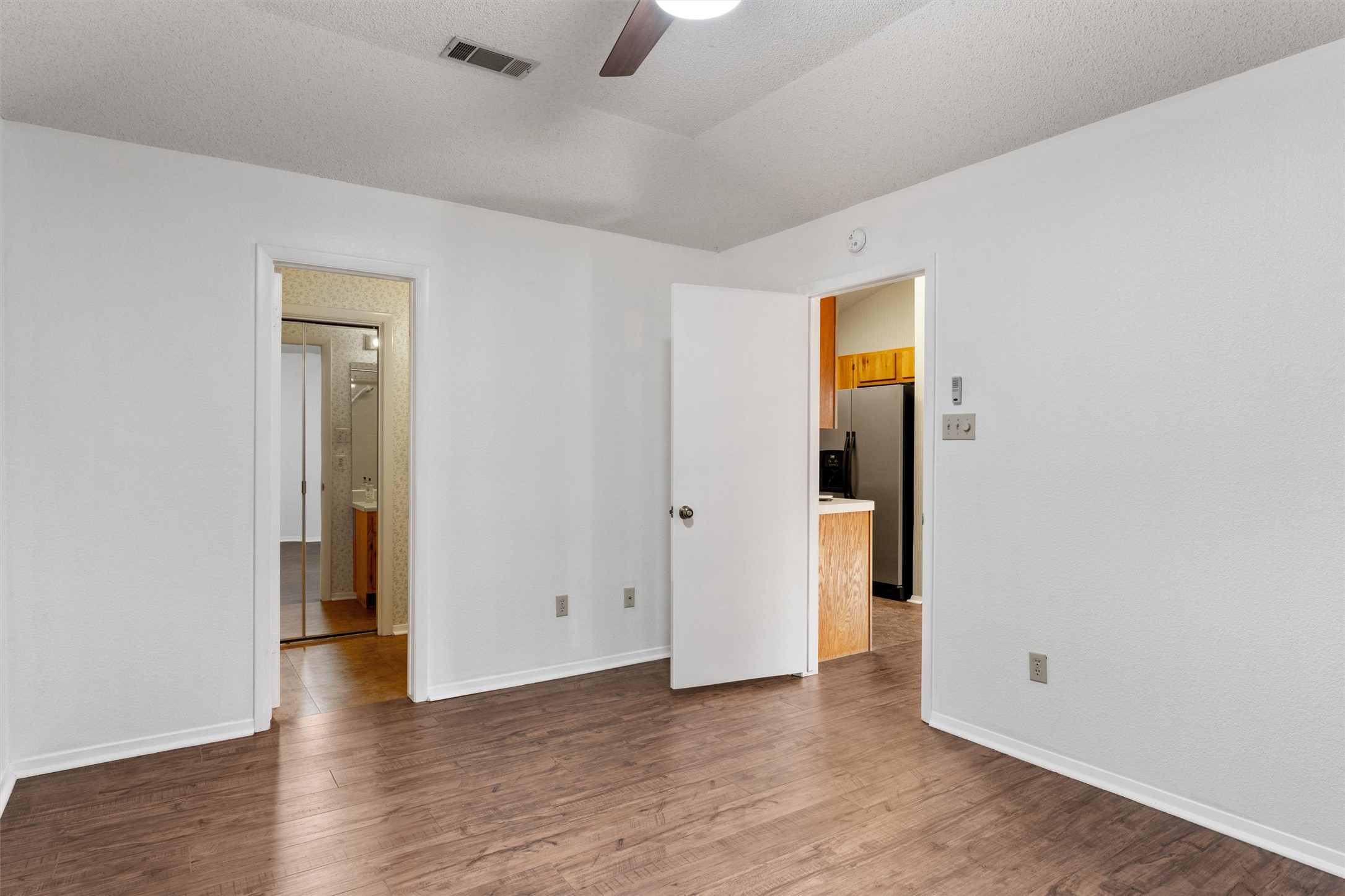 12314 Furrow Cove, Unit A Austin, TX 78753 - Photo 11 of 23 Unfurnished bedroom featuring a textured ceiling, a ceiling fan, dark wood finished floors, stainless steel refrigerator with ice dispenser, and lofted ceiling