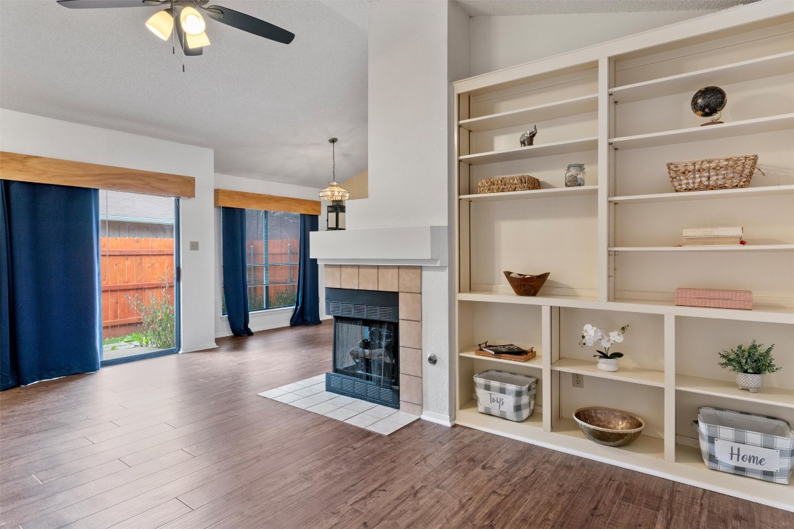 12314 Furrow Cove, Unit A Austin, TX 78753 - Photo 3 of 23 Unfurnished living room featuring wood finished floors, a tiled fireplace, vaulted ceiling, and ceiling fan