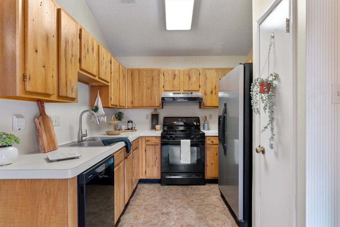 12314 Furrow Cove, Unit A Austin, TX 78753 - Photo 8 of 23 Kitchen with black appliances, light countertops, under cabinet range hood, and a textured ceiling
