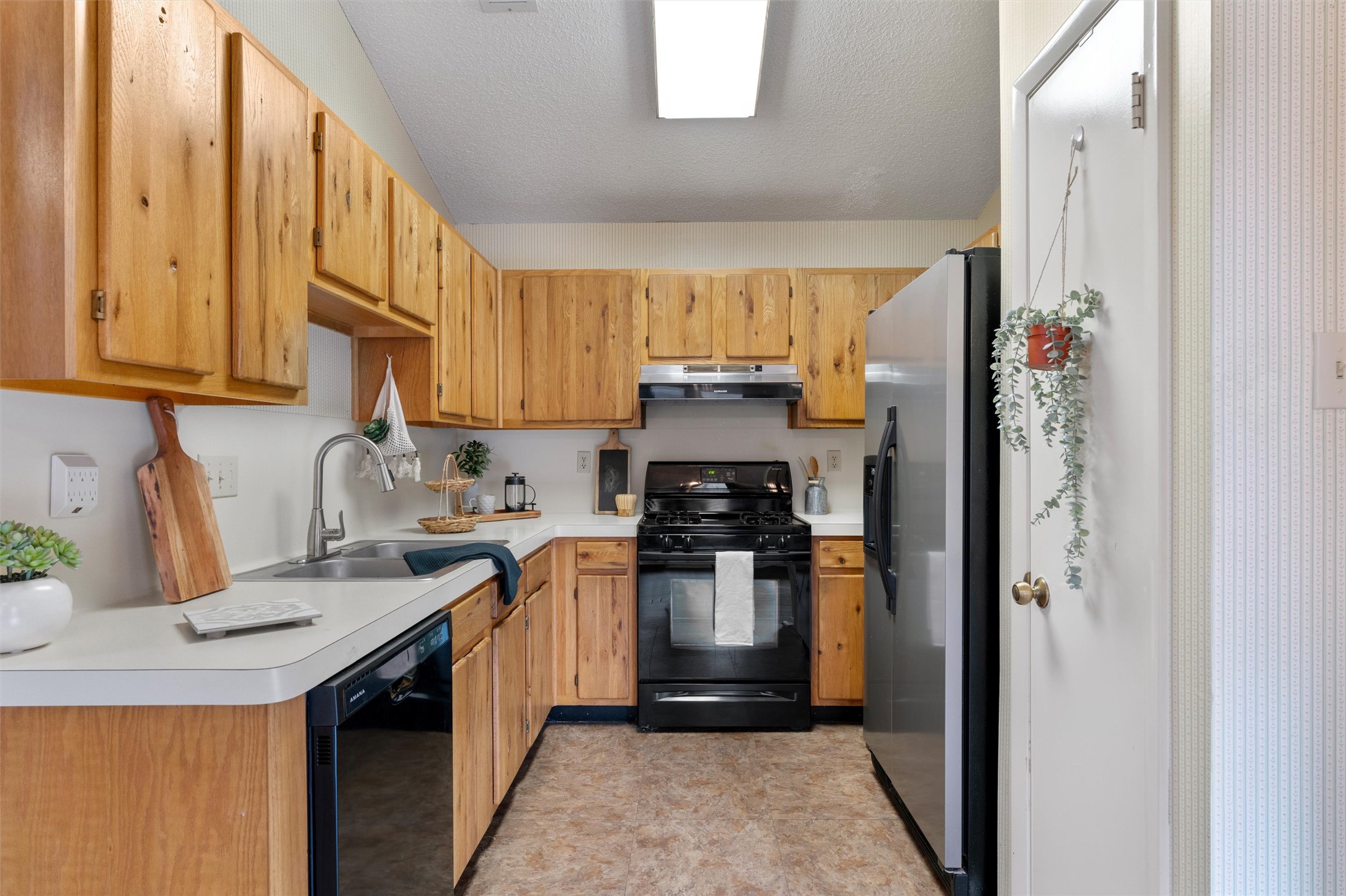 12314 Furrow Cove, Unit A Austin, TX 78753 - Photo 8 of 23 Kitchen with black appliances, light countertops, under cabinet range hood, and a textured ceiling