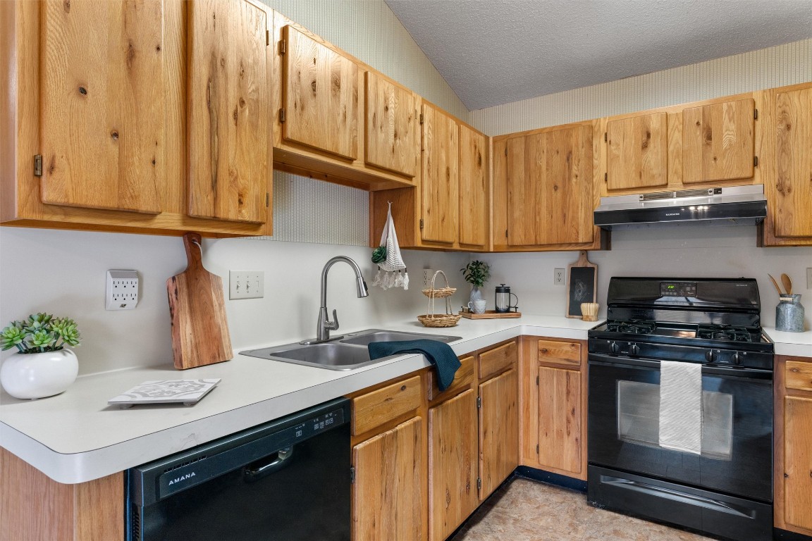 12314 Furrow Cove, Unit A Austin, TX 78753 - Photo 9 of 23 Kitchen featuring black appliances, light countertops, under cabinet range hood, a textured ceiling, and brown cabinetry