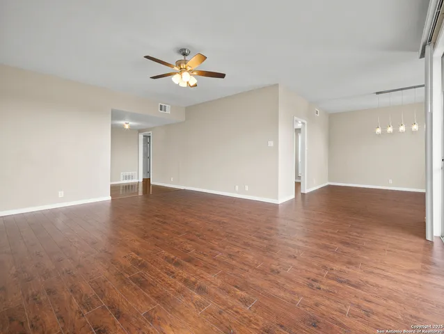 a view of an empty room with wooden floor and a ceiling fan