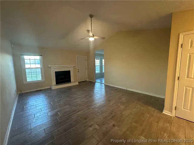an empty room with wooden floor fireplace and windows