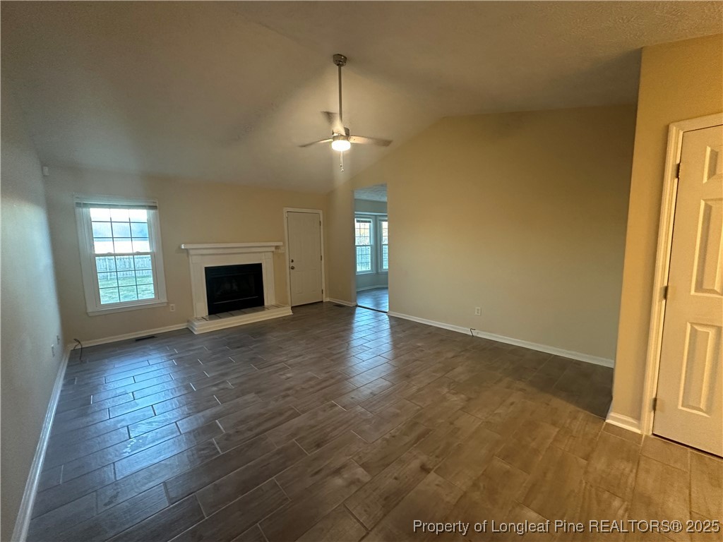 8249 Rockfish Road Raeford, NC 28376 - Photo 2 of 12 an empty room with wooden floor fireplace and windows