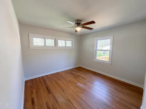 a view of empty room with wooden floor and fan