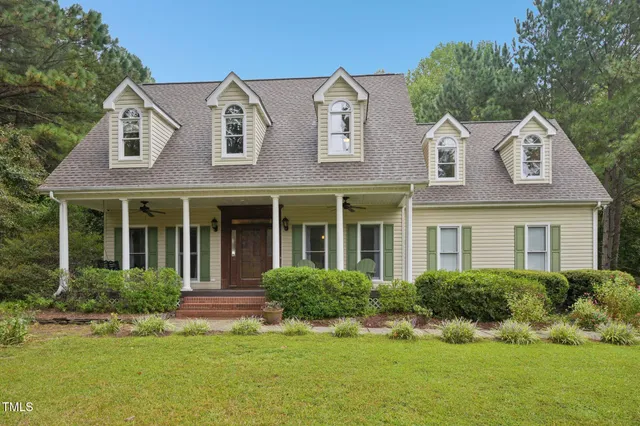 a view of a white house with a big yard and potted plants and large trees