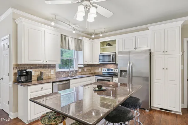 a kitchen with stainless steel appliances granite countertop a stove refrigerator a sink dishwasher and white cabinets with wooden floor