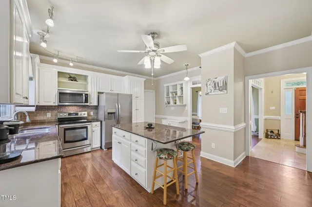 a kitchen with stainless steel appliances granite countertop a stove top oven a sink a dining table and chairs with wooden floor