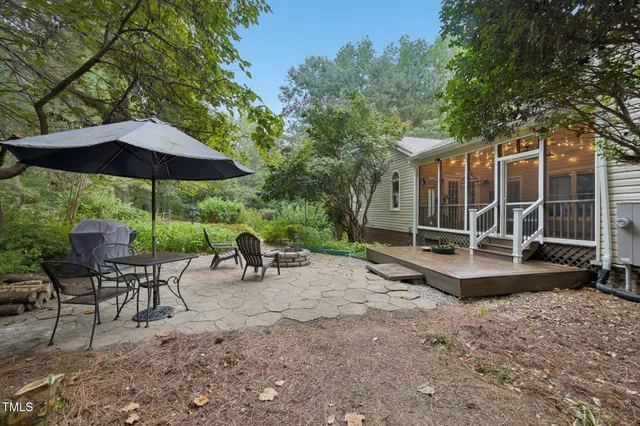 a view of backyard with table and chairs under an umbrella with large trees