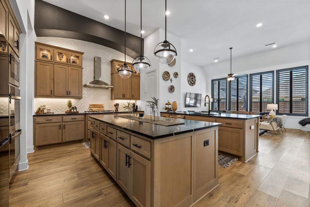 Kitchen with hanging light fixtures, a kitchen island with sink, light wood-type flooring, ceiling fan, and wall chimney exhaust hood
