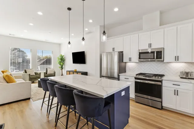 a kitchen with stainless steel appliances a stove a sink a microwave a refrigerator a stove a dining table and chairs with wooden floor