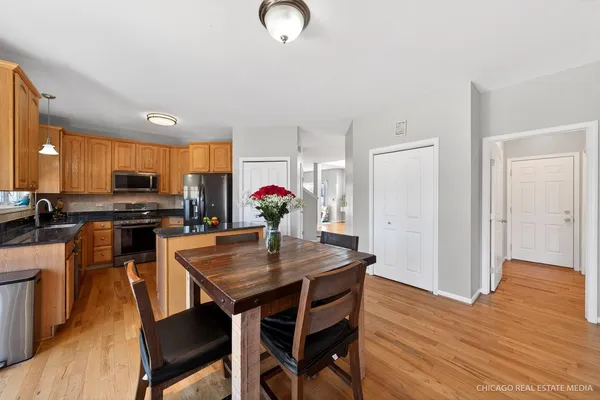 a kitchen with stainless steel appliances granite countertop a stove top oven a refrigerator a dining table and chairs with wooden floor