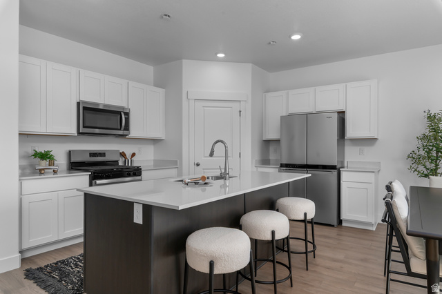 2819 South 710th West, Unit 14 Logan, UT 84321 - Photo 13 of 24 Modern kitchen featuring a central island with a sink, stainless steel appliances, light wood-finish flooring, white cabinetry, and light-toned countertops