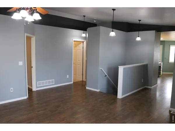 a view of an empty room with wooden floor and a ceiling fan