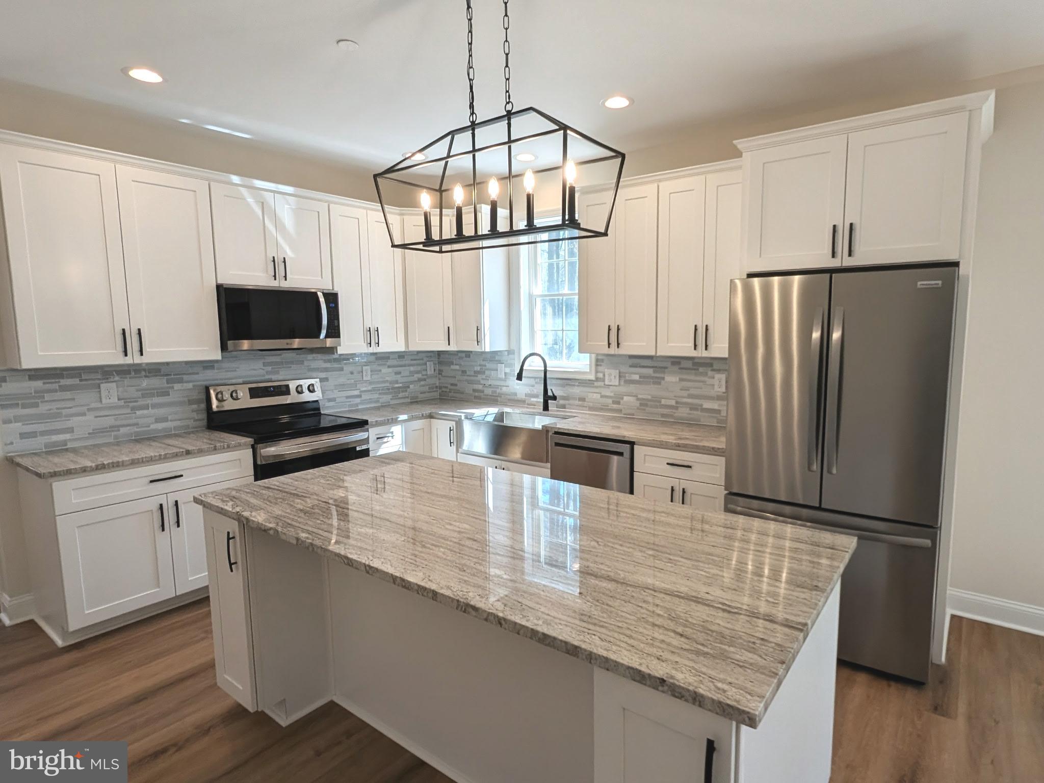 a kitchen with kitchen island granite countertop a refrigerator oven a sink dishwasher and white cabinets with wooden floor