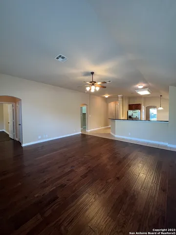 a view of an empty room with wooden floor and a kitchen