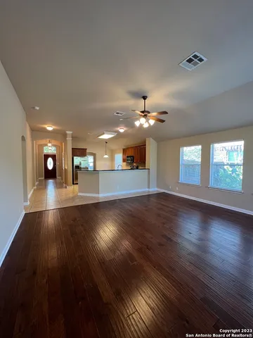 a view of an empty room with wooden floor and a kitchen