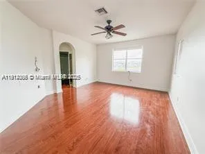 an empty room with wooden floor fan and windows