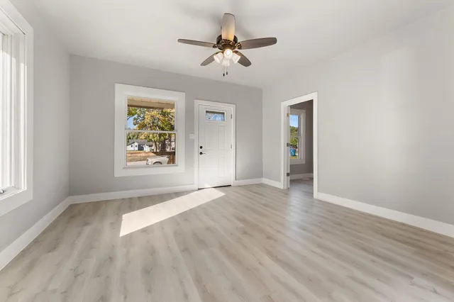 an empty room with wooden floor chandelier fan and windows