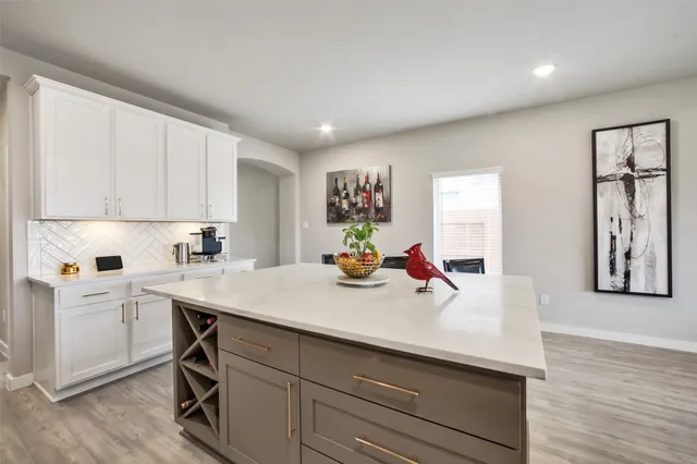 a view of a kitchen with kitchen island a stove a sink a refrigerator and white cabinets with wooden floor