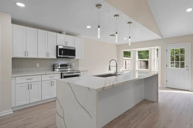 a kitchen with stainless steel appliances granite countertop a stove top oven a sink a refrigerator white cabinets and wooden floor