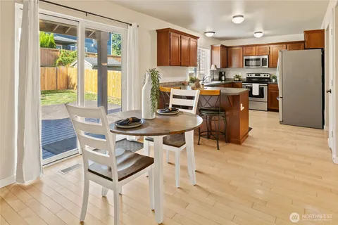 a open kitchen with stainless steel appliances granite countertop a stove top oven a refrigerator a dining table and chairs with wooden floor