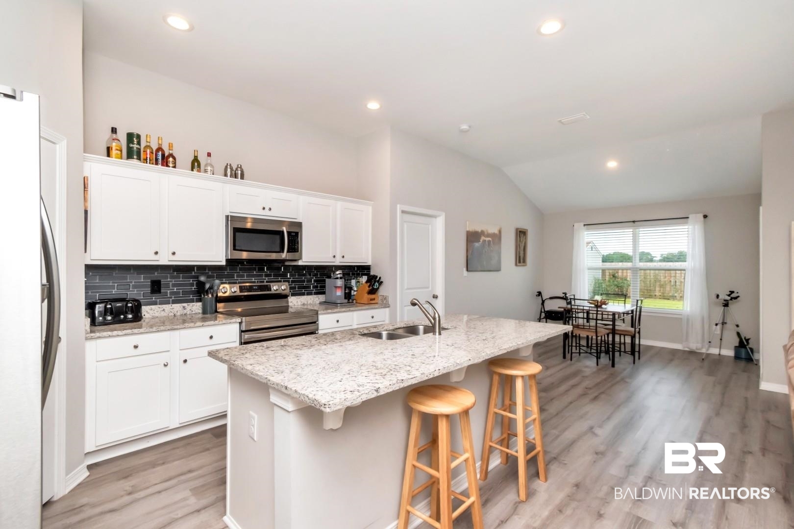 1295 Hayward Loop Foley, AL 36535 - Photo 9 of 29 Contemporary kitchen featuring white cabinetry, stainless steel appliances, a dark subway tile backsplash, and a spacious island with a double sink and granite-finish countertop