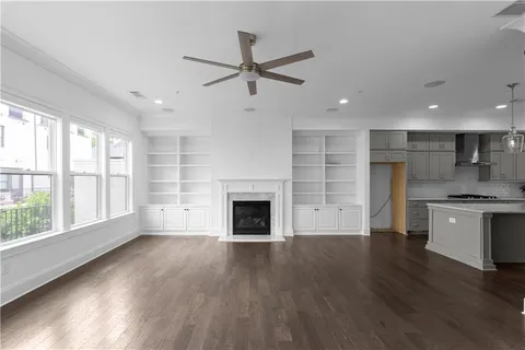 an empty room with wooden floor a ceiling fan and a kitchen view
