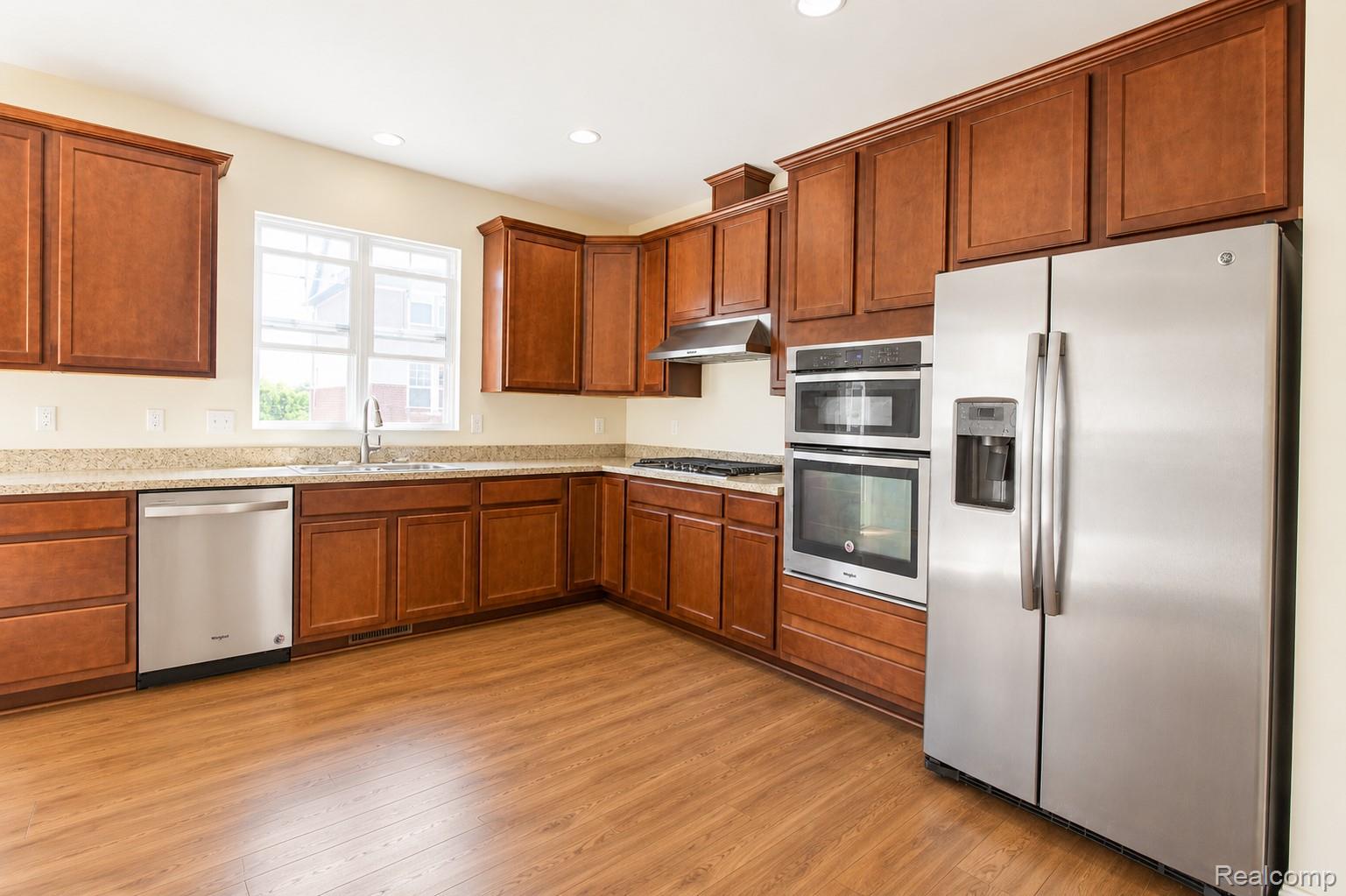 2940 Glenbar Circle Rochester, MI 48307 - Photo 6 of 15 Kitchen featuring wood-finish flooring, ample wood cabinetry, light-toned countertops, and stainless steel appliances including a double-door refrigerator, double oven, and dishwasher