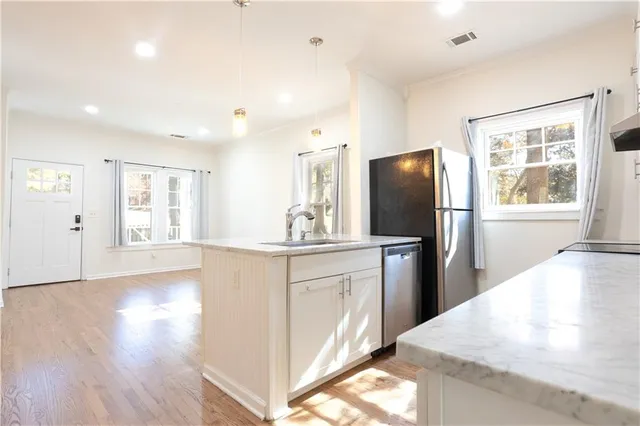 a kitchen with stainless steel appliances granite countertop a refrigerator a sink a stove and white cabinets with wooden floor