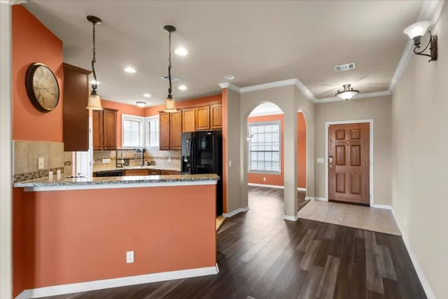 a open kitchen with stainless steel appliances granite countertop a refrigerator a oven a sink and a dining table with wooden floor