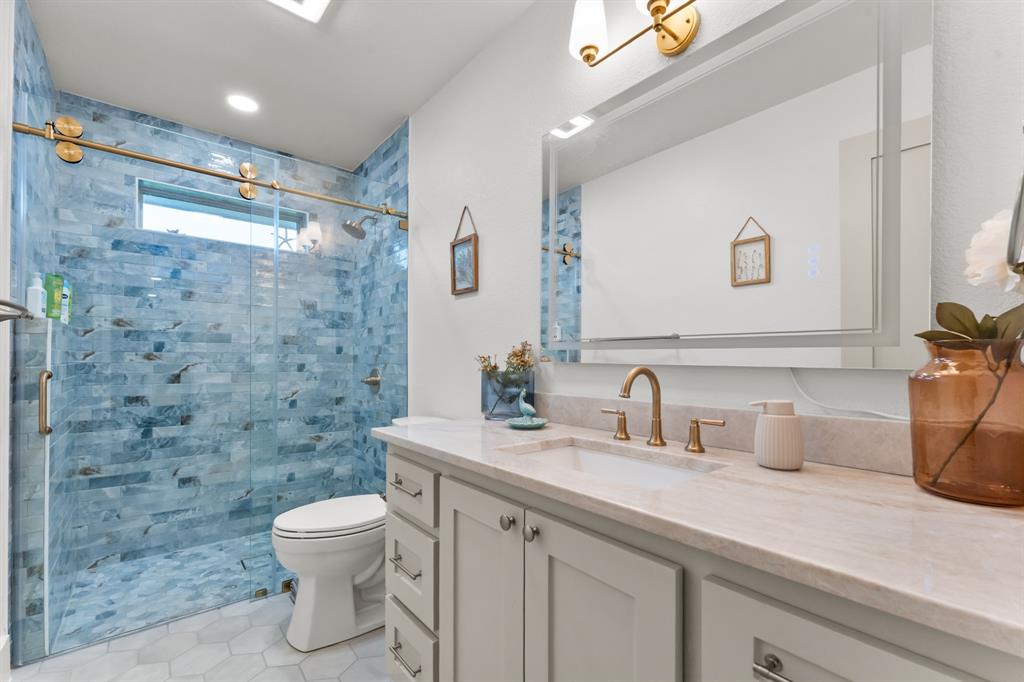380 Farr Altom Road Seagoville, TX 75159 - Photo 18 of 30 Bathroom featuring a frameless glass shower enclosure with brass hardware, blue stone-look tile shower surround, hexagon floor tiles, and a white vanity with a stone countertop and brass faucet